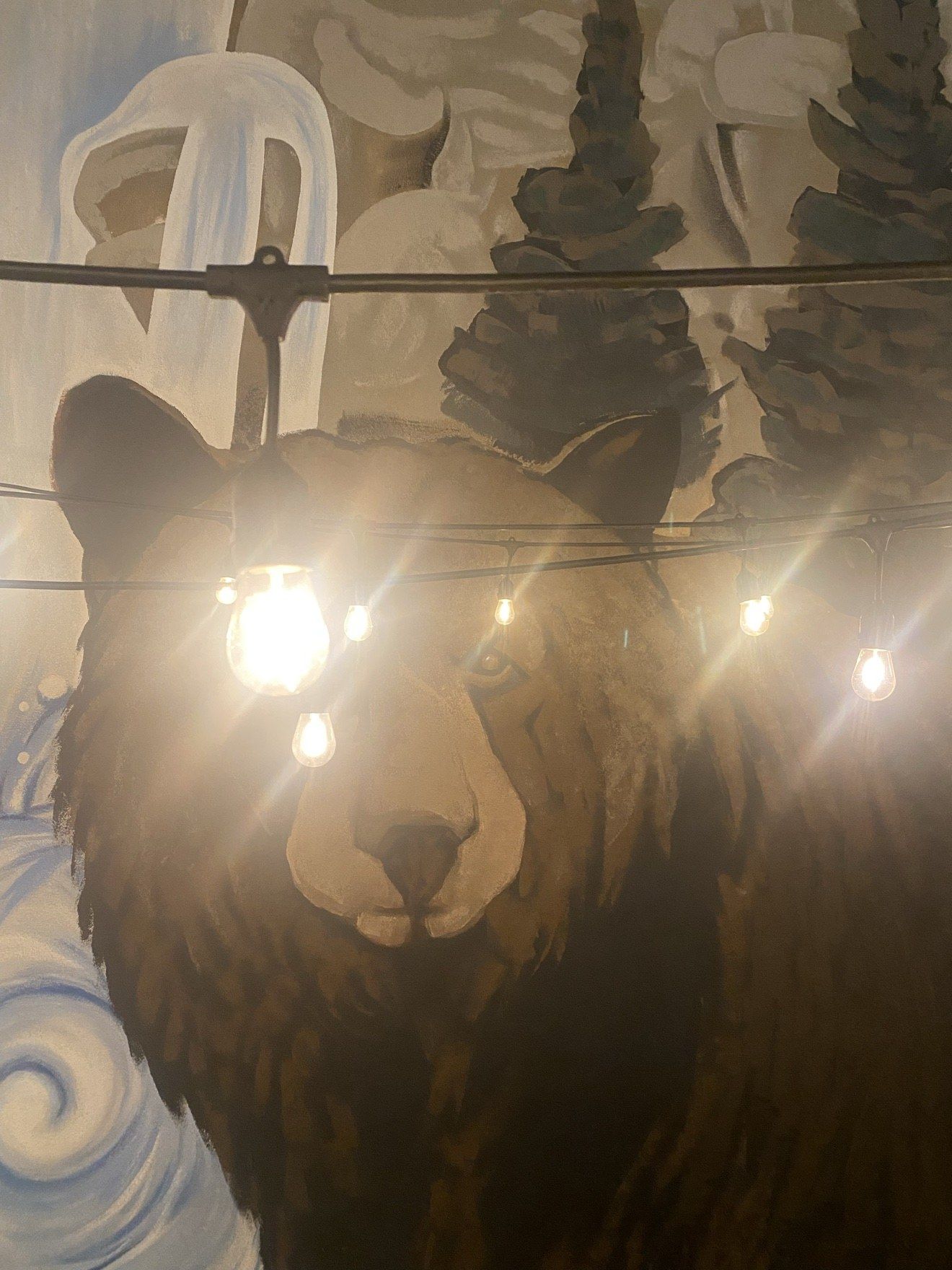 The bear mural on the Lighthouse 971 patio at night, lit by string lights